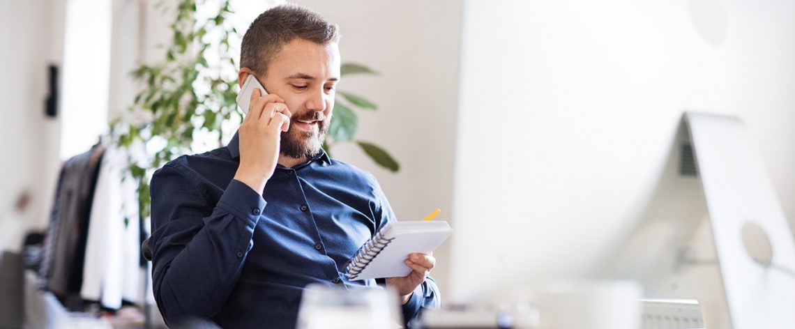 Man on the mobile in office reading a notepad