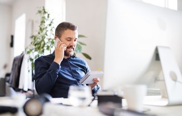 Man on the mobile in office reading a notepad