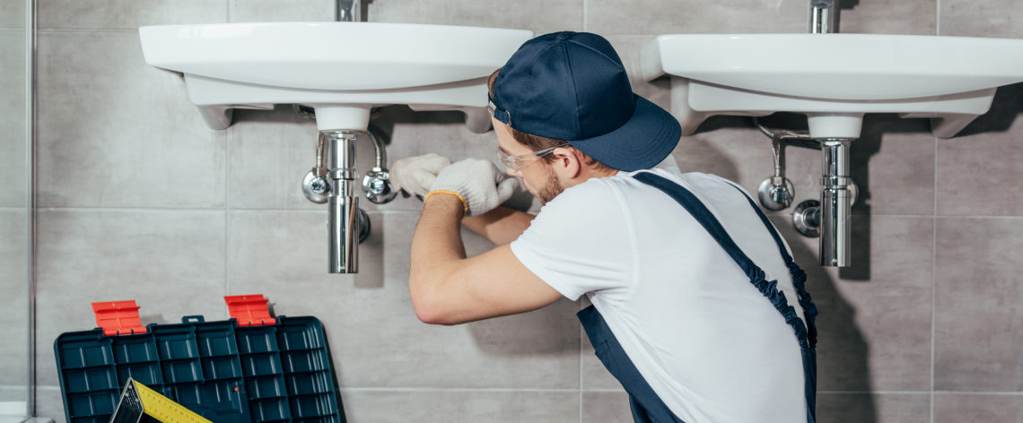 back view of young professional plumber fixing sink in bathroom