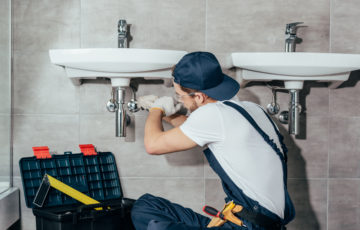 back view of young professional plumber fixing sink in bathroom