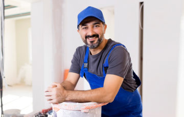 painter leaning on paint can facing the camera